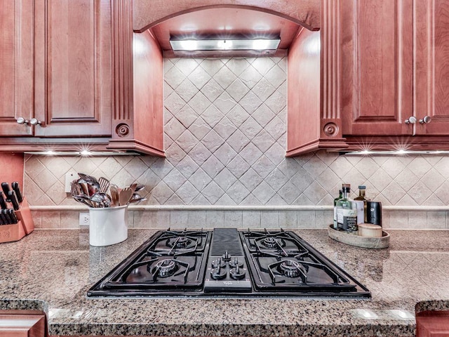 kitchen with arched walkways, stovetop with downdraft, backsplash, and light stone countertops