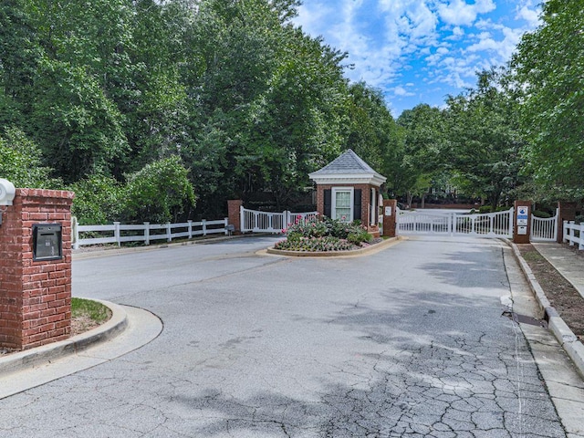 view of asphalt road featuring curbs, a gate, and a gated entry