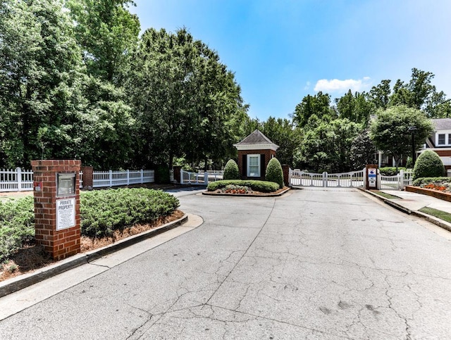 view of asphalt street with a gate, curbs, a gated entry, view of scattered trees, and sidewalks