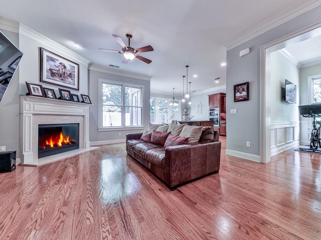 living room featuring a fireplace, ceiling fan, light wood finished floors, ornamental molding, and baseboards