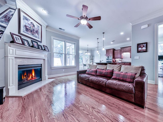 living area featuring wood finished floors, a ceiling fan, a premium fireplace, baseboards, and ornamental molding