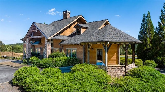 view of front of home featuring a chimney, roof with shingles, and stone siding