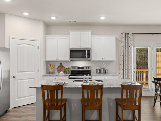 kitchen featuring stainless steel appliances, a sink, decorative backsplash, white cabinetry, and recessed lighting