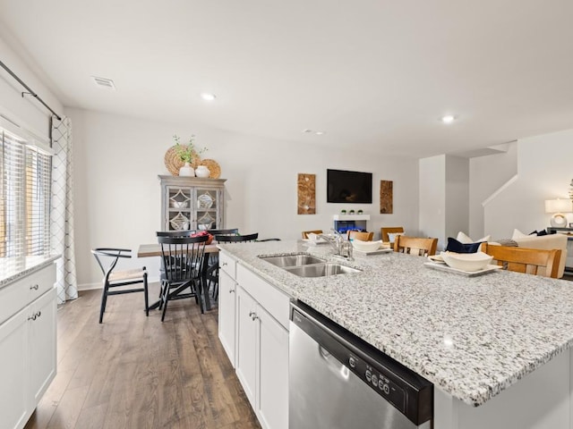 kitchen with stainless steel dishwasher, a sink, open floor plan, an island with sink, and white cabinetry