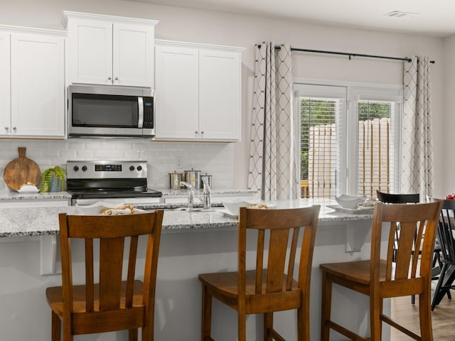 kitchen with stainless steel appliances, backsplash, white cabinets, and light stone countertops