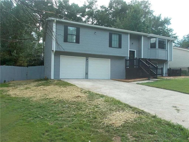 raised ranch featuring concrete driveway, an attached garage, a front lawn, and fence