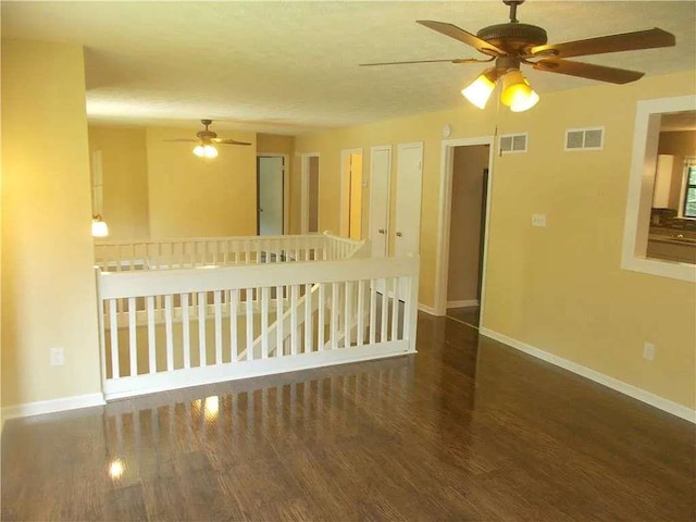 empty room with a ceiling fan, baseboards, visible vents, and wood finished floors