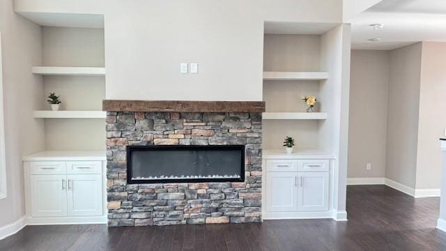 unfurnished living room featuring dark wood finished floors, a stone fireplace, built in shelves, and baseboards