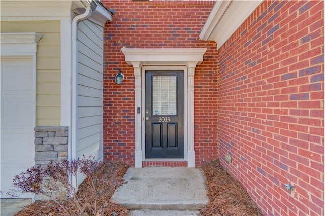 view of exterior entry with a garage and brick siding