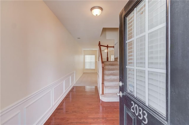 hall with stairway, a wainscoted wall, dark wood-style flooring, and a decorative wall