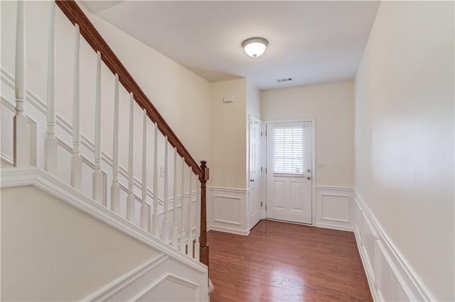 doorway with visible vents, stairs, wainscoting, wood finished floors, and a decorative wall