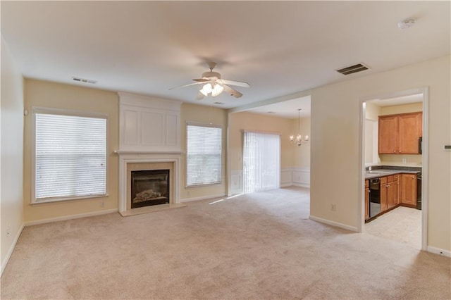 unfurnished living room with visible vents, light carpet, a large fireplace, and ceiling fan with notable chandelier