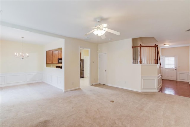 interior space featuring light carpet, a decorative wall, ceiling fan with notable chandelier, and a wainscoted wall