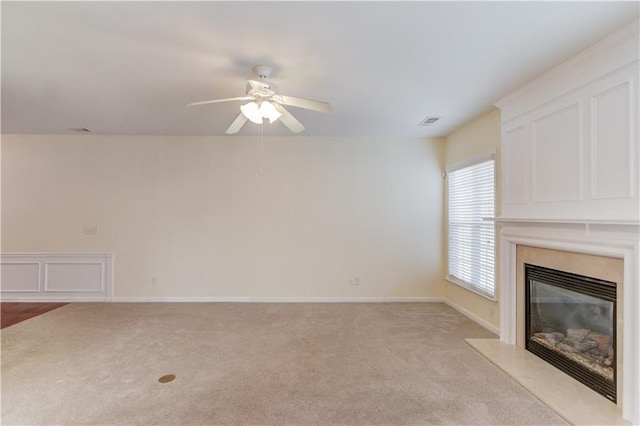 unfurnished living room featuring a ceiling fan, baseboards, visible vents, a premium fireplace, and light colored carpet