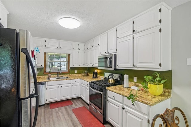 kitchen with white cabinetry, light wood-type flooring, stainless steel appliances, light stone countertops, and sink