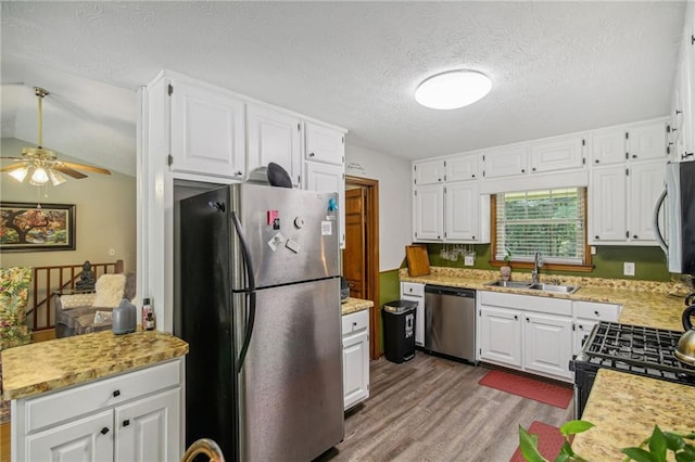 kitchen with appliances with stainless steel finishes, white cabinets, sink, light hardwood / wood-style floors, and ceiling fan