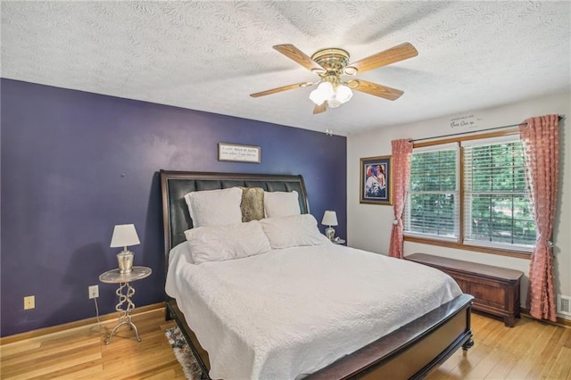 bedroom with a textured ceiling, ceiling fan, and light hardwood / wood-style floors