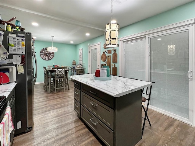 kitchen featuring a breakfast bar, dark wood-type flooring, decorative light fixtures, a kitchen island, and stainless steel refrigerator