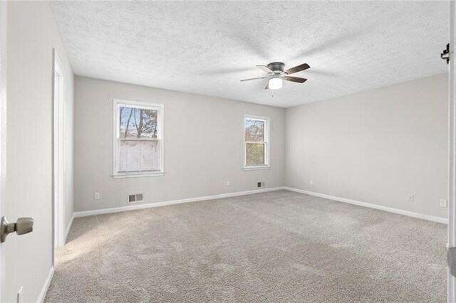 carpeted empty room with ceiling fan, a textured ceiling, and a wealth of natural light