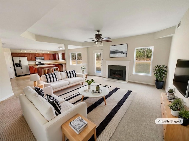 living area with visible vents, baseboards, a fireplace with flush hearth, ceiling fan, and light colored carpet