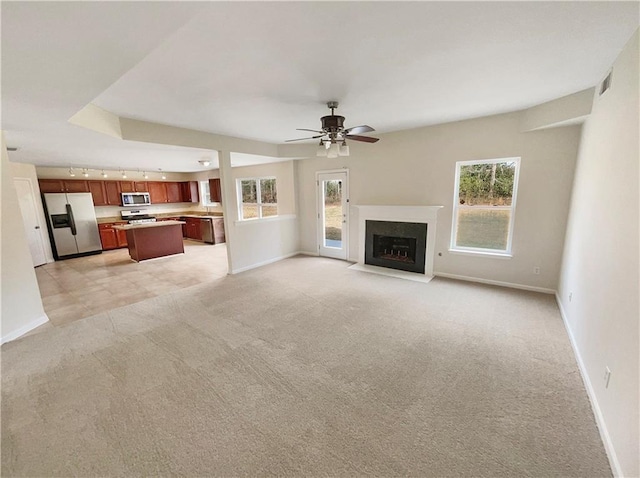 unfurnished living room with a fireplace with flush hearth, baseboards, light colored carpet, and a ceiling fan