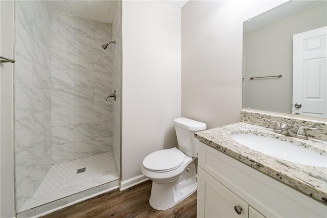 bathroom with tiled shower, hardwood / wood-style floors, vanity, and toilet