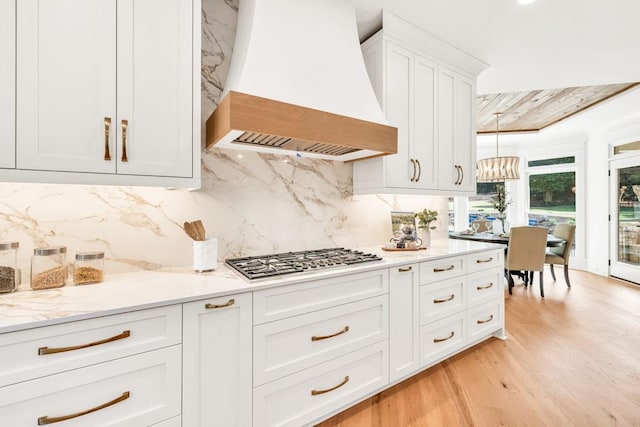 2335 Flat Stone Dr, Cumming, GA 30041 - kitchen with light wood finished floors, an inviting chandelier, backsplash, stainless steel gas stovetop, and custom exhaust hood
