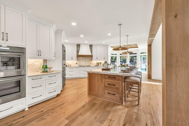 2335 Flat Stone Dr, Cumming, GA 30041 - kitchen featuring appliances with stainless steel finishes, backsplash, white cabinets, custom range hood, and light wood-style floors