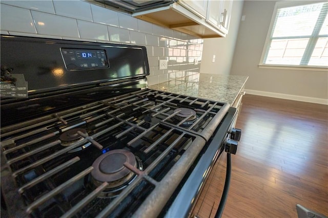 2034 W Hampton Dr, Canton, GA 30115 - details with black range with gas stovetop, dark wood finished floors, light stone countertops, tasteful backsplash, and baseboards