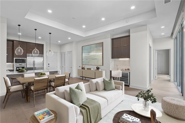 living room with beverage cooler, light wood-type flooring, and a tray ceiling