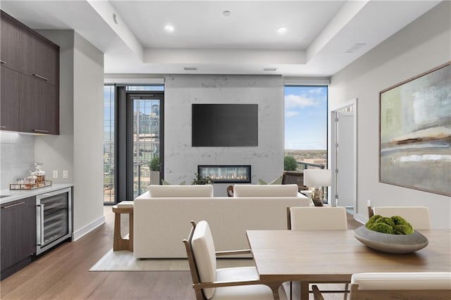 dining room featuring a high end fireplace, beverage cooler, wood-type flooring, and a raised ceiling