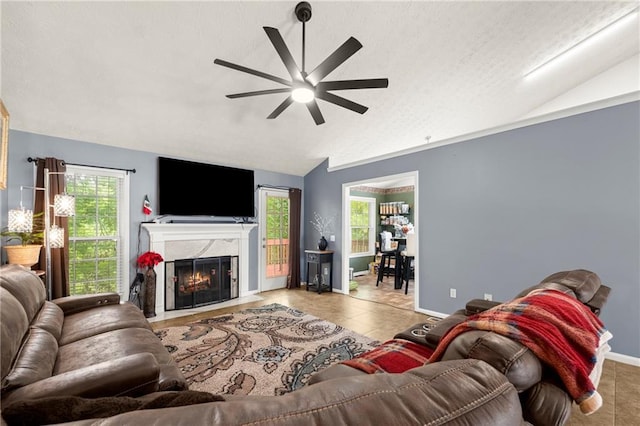 living area with a fireplace, light tile patterned floors, lofted ceiling, a ceiling fan, and baseboards