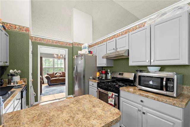 kitchen featuring appliances with stainless steel finishes, light countertops, under cabinet range hood, white cabinetry, and a notable chandelier