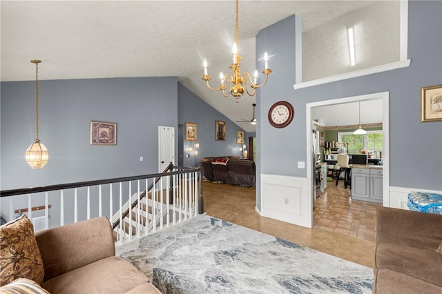 living room with a notable chandelier, a decorative wall, wainscoting, high vaulted ceiling, and tile patterned flooring