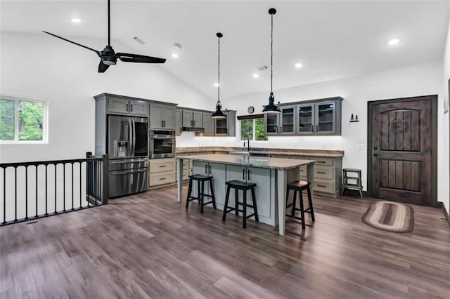 kitchen with appliances with stainless steel finishes, a kitchen breakfast bar, healthy amount of natural light, a ceiling fan, and high vaulted ceiling