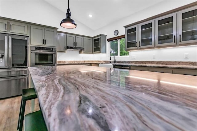 kitchen with appliances with stainless steel finishes, a sink, lofted ceiling, light stone counters, and pendant lighting