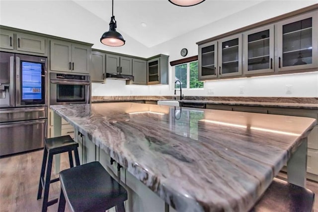 kitchen featuring stainless steel fridge, lofted ceiling, a kitchen breakfast bar, stone countertops, and under cabinet range hood