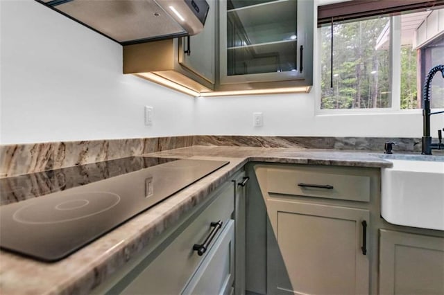 kitchen featuring range hood, black electric cooktop, a sink, light stone countertops, and gray cabinets