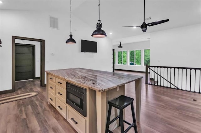 kitchen with black microwave, dark wood finished floors, a kitchen breakfast bar, light stone countertops, and vaulted ceiling