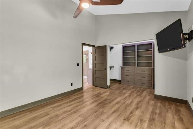unfurnished bedroom with baseboards, light wood finished floors, a towering ceiling, and ceiling fan