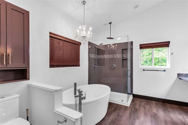 full bathroom featuring a shower stall, a chandelier, a freestanding bath, wood finished floors, and toilet