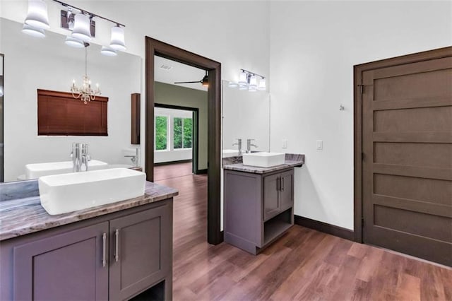bathroom with two vanities, wood finished floors, a chandelier, and baseboards