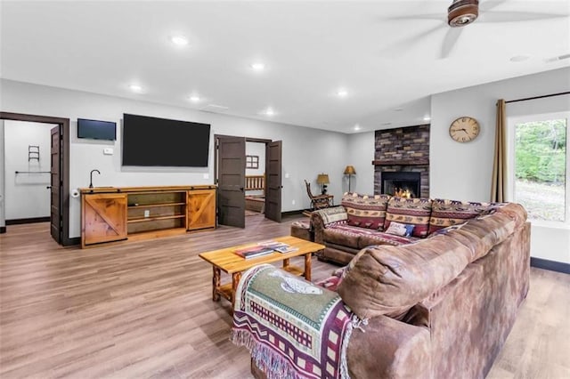 living room featuring light wood-style floors, baseboards, recessed lighting, a stone fireplace, and ceiling fan