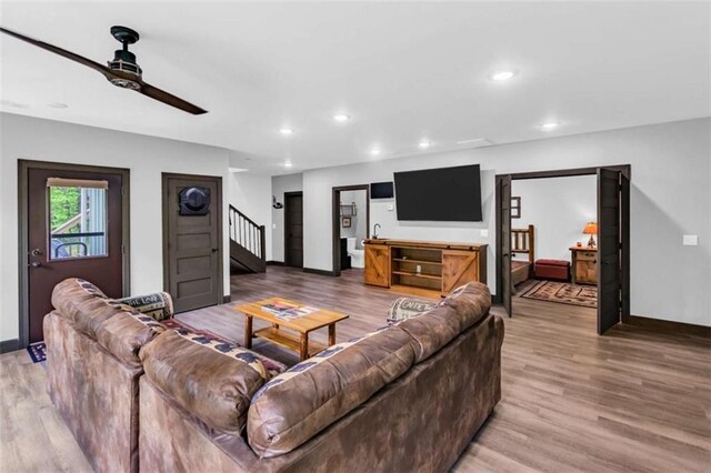 living room with light wood finished floors, a ceiling fan, stairs, baseboards, and recessed lighting