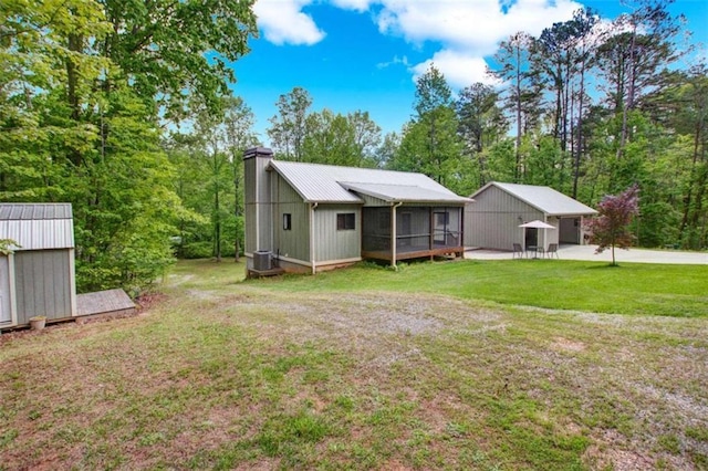 back of property featuring a lawn, a chimney, an outbuilding, a sunroom, and a patio
