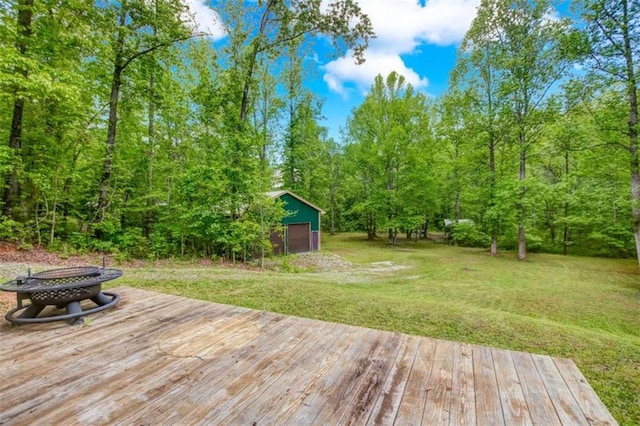 wooden deck featuring a fire pit, a lawn, and an outbuilding