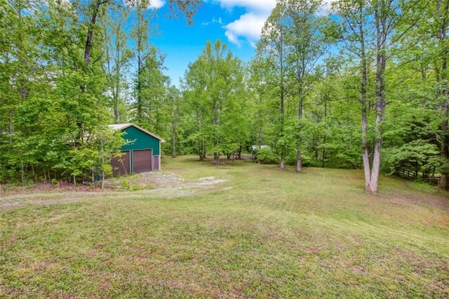 view of green lawn featuring a detached garage, an outbuilding, a pole building, and a wooded view