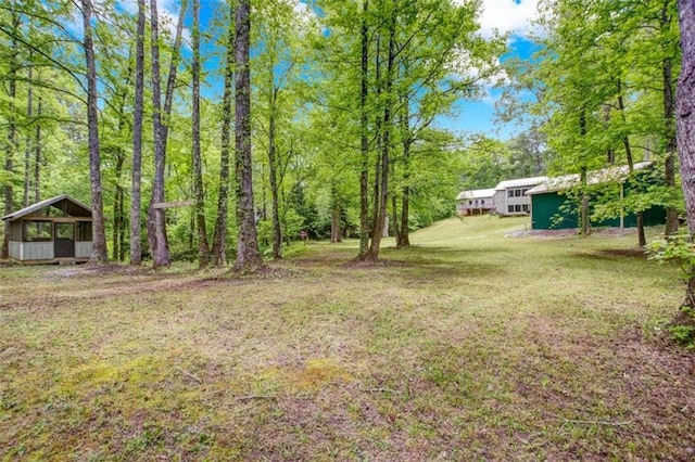 view of green lawn with a sunroom and a wooded view