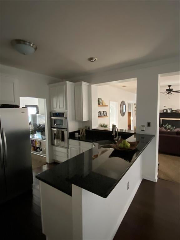 kitchen with white cabinets, dark countertops, freestanding refrigerator, a peninsula, and a sink