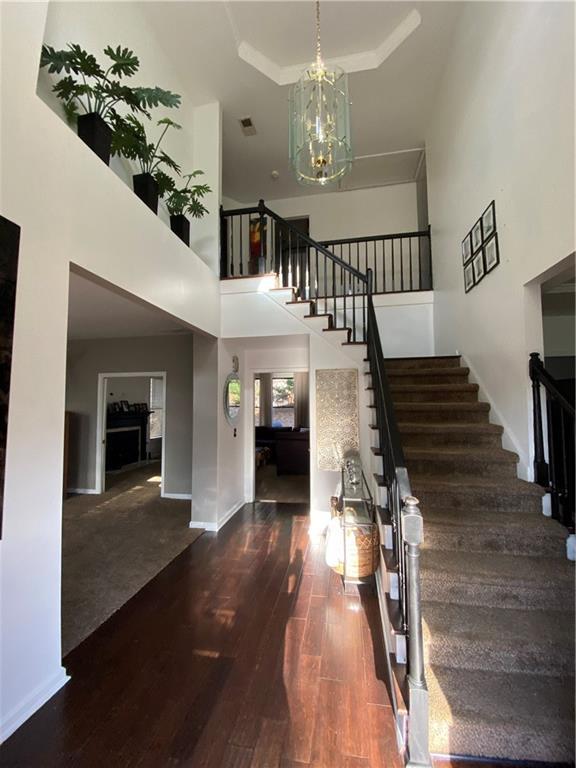 entryway with a tray ceiling, stairway, a high ceiling, an inviting chandelier, and wood finished floors